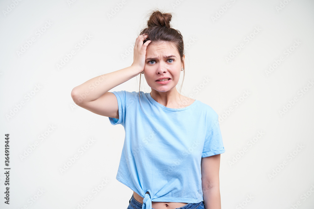 Indoor photo of young brunette lady dressed in casual wear holding palm on her head and grimacing face while looking at camera, isolated over white background Indoor photo of young brunette lady dressed in casual wear holding palm on her head and grimacing face while looking at camera, isolated over white background