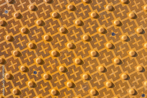фотографія Closeup of yellow geometric pattern of micro-pyramids in cruciform arrays alternating with round bumps having tiny pyramid arrays on their tops