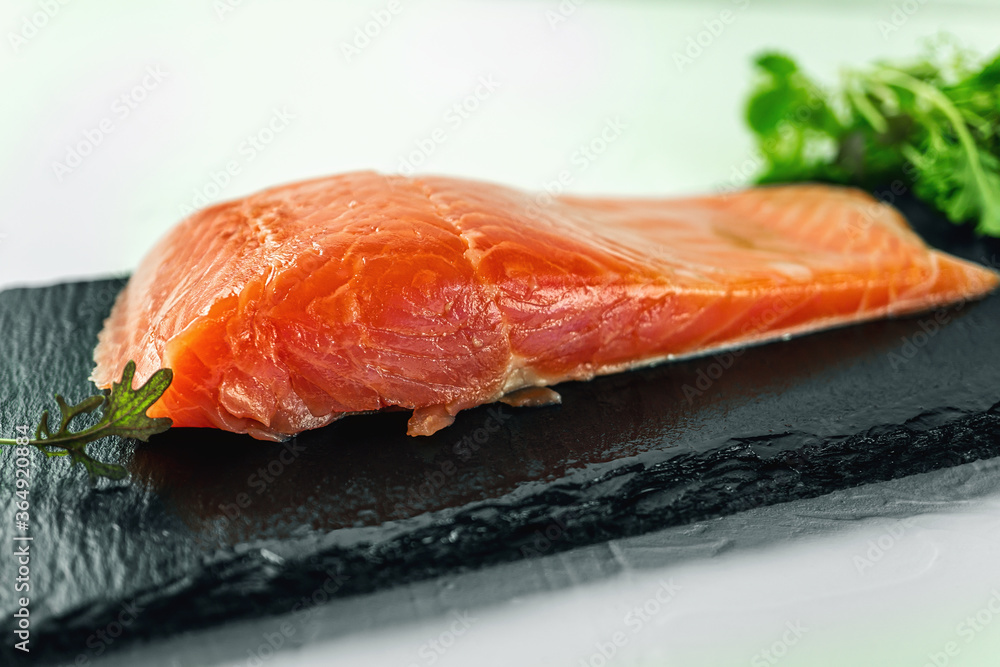 piece of smoked fresh salmon with lettuce leaves on a slate Board