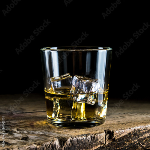 A glass of whiskey with ice cubes on a wooden table and a dark background
