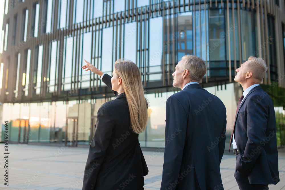 Agent and customers meeting outdoors, discussing real property, pointing at office building. Back view. Commercial real estate concept Agent and customers meeting outdoors, discussing real property, pointing at office building. Back view. Commercial real estate concept