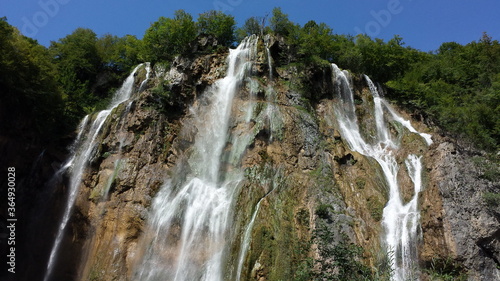 Waterfalls in Plitvica park, water falling from top of the hill with trees on top of it. 