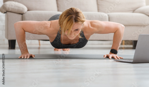 Push ups at home. Adult woman doing fitness exercises on floor mat with laptop