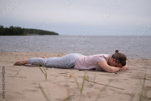 Sporty woman relaxing in yoga asana Makarasana or crocodile pose sitting on beach