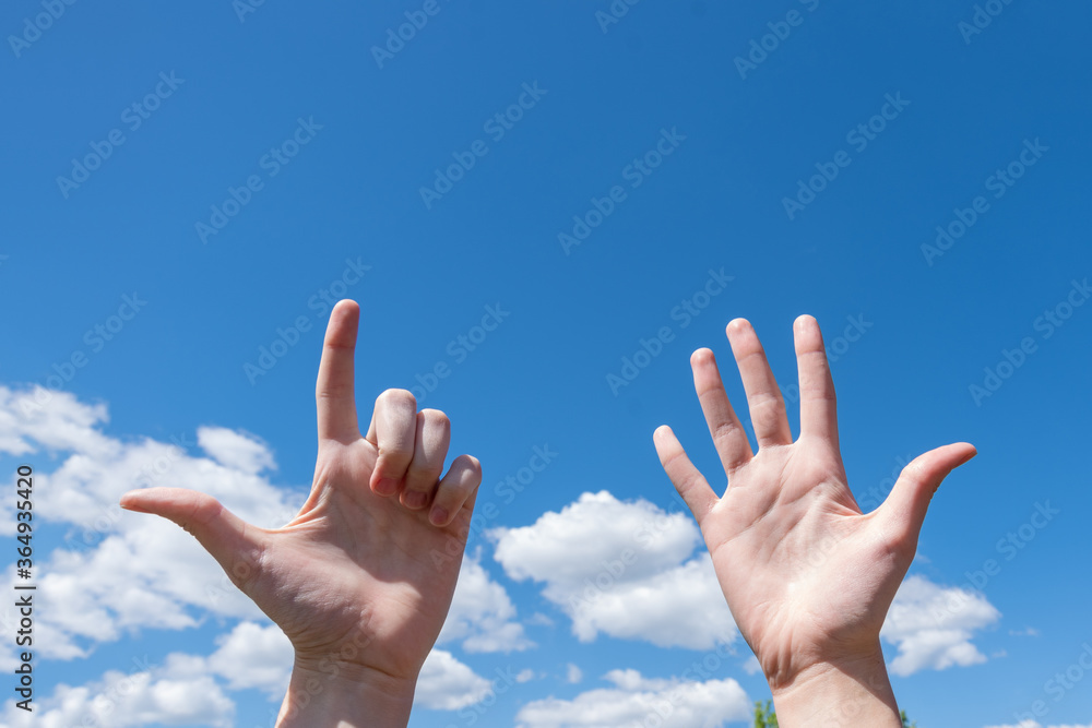 Gesture closeup of a woman's hand showing one open palm and two fingers up isolated on a blue sky background