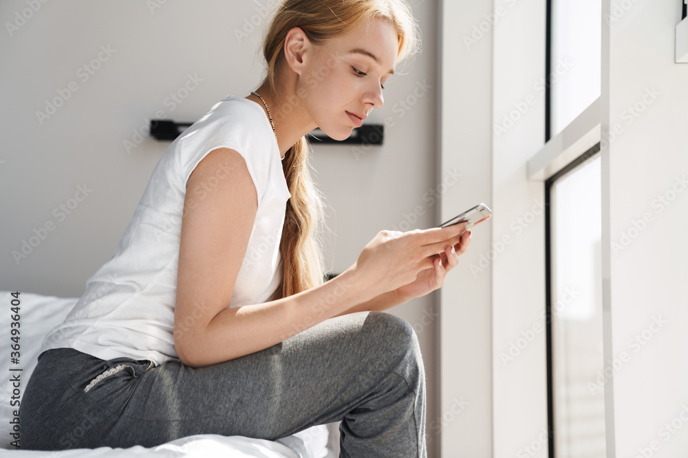 Photo of focused young woman using cellphone while sitting in bed Photo of focused young woman using cellphone while sitting in bed