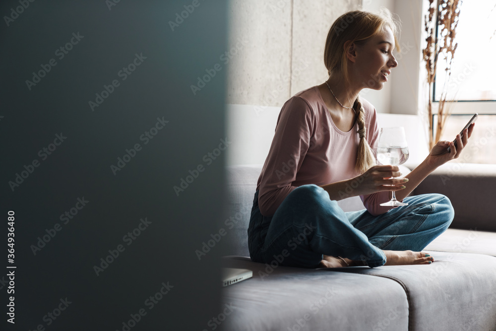 Photo ofwoman using cellphone and drinking water while sitting on sofa Photo ofwoman using cellphone and drinking water while sitting on sofa