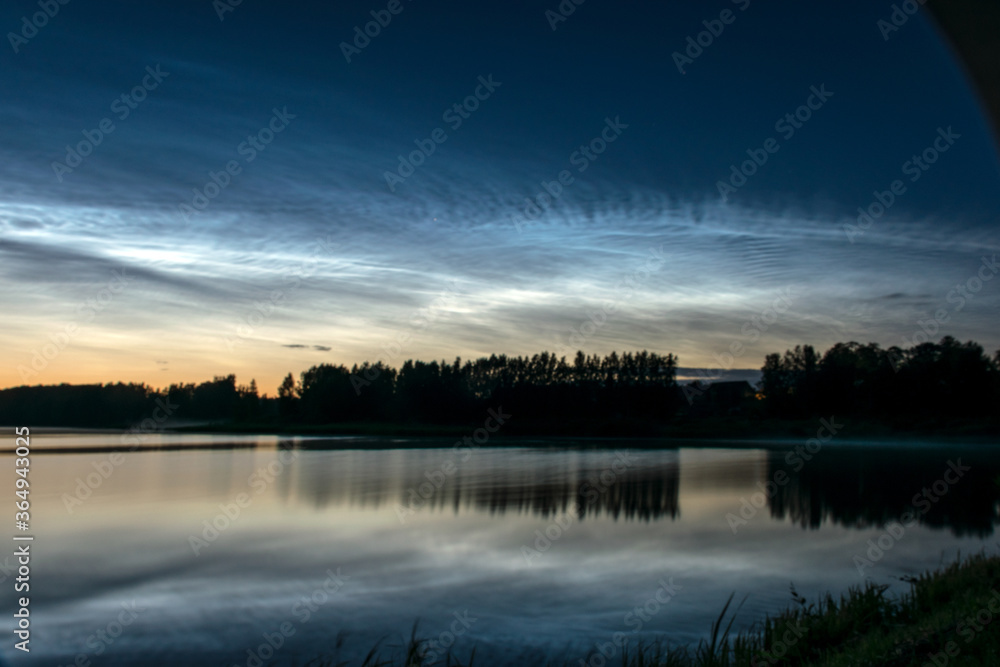 night landscape with white silver clouds over the lake, blurred foreground, charming cloud reflections in the lake water, summer night