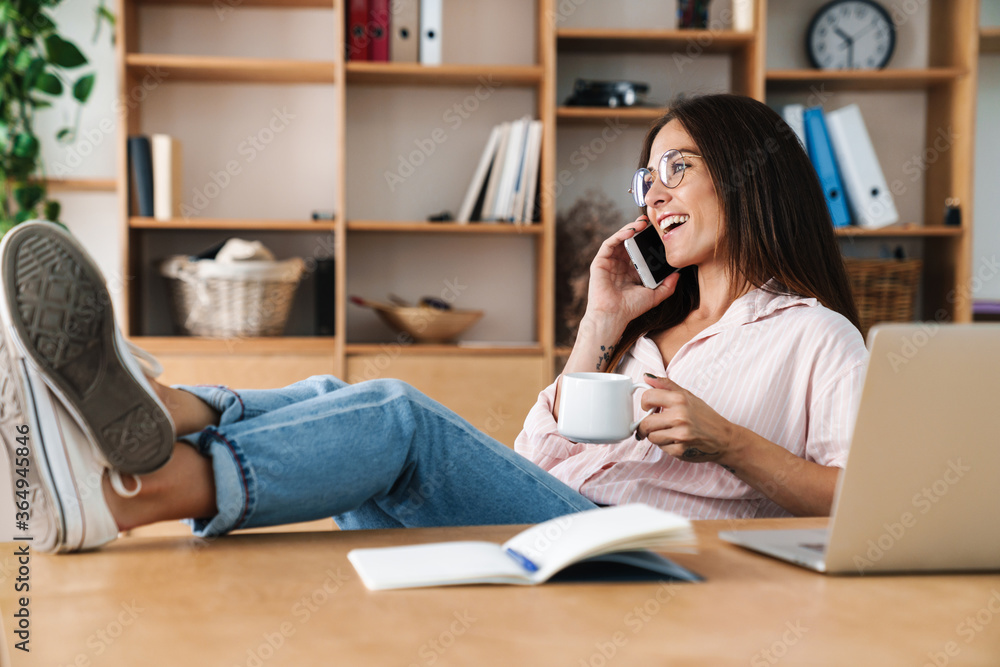 Image of smiling businesswoman talking on cellphone and drinking coffee Image of smiling businesswoman talking on cellphone and drinking coffee