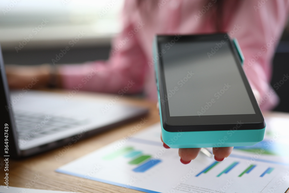 Close-up of businesswoman holding machine for contactless payment. Stylish female sitting on working table in office. Paper on desk. Modern technology and innovation concept Close-up of businesswoman holding machine for contactless payment. Stylish female sitting on working table in office. Paper on desk. Modern technology and innovation concept