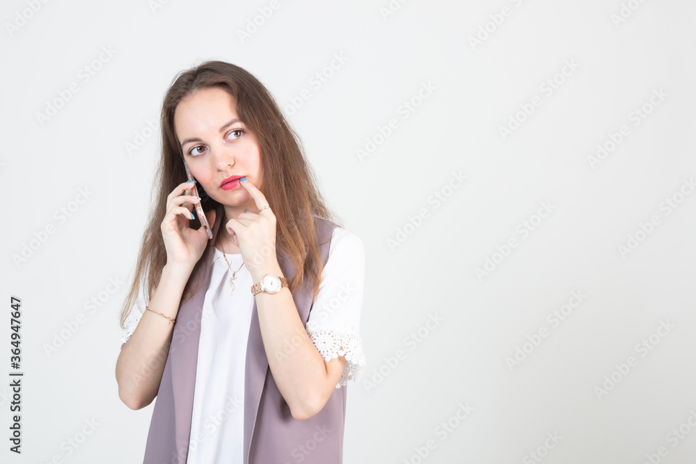 beautiful young woman in business strict clothes poses against a white wall with a phone in her hands beautiful young woman in business strict clothes poses against a white wall with a phone in her hands