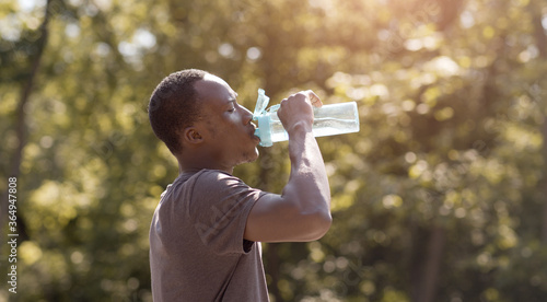 Overheated black guy drinking water from bottle in park photo