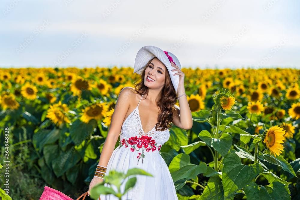 Beautiful woman poses in the agricultural field with sunflower on a sunny summer day