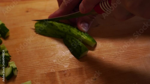 Men's hands slice fresh cucumber on a wooden board
