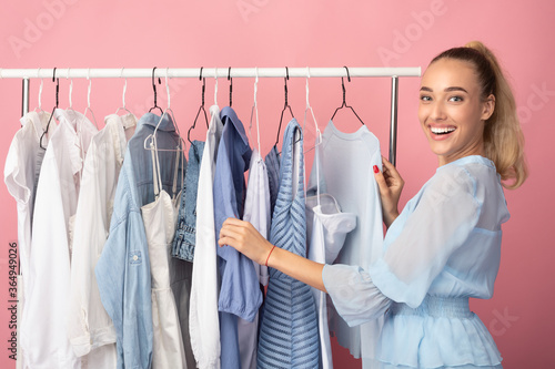 Portrait of cheerful girl choosing clothes standing near rack