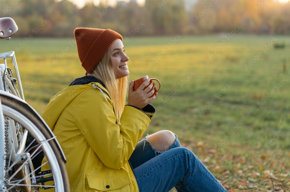 Φωτογραφία Beautiful smiling woman sitting on grass in park, holding cup of coffee