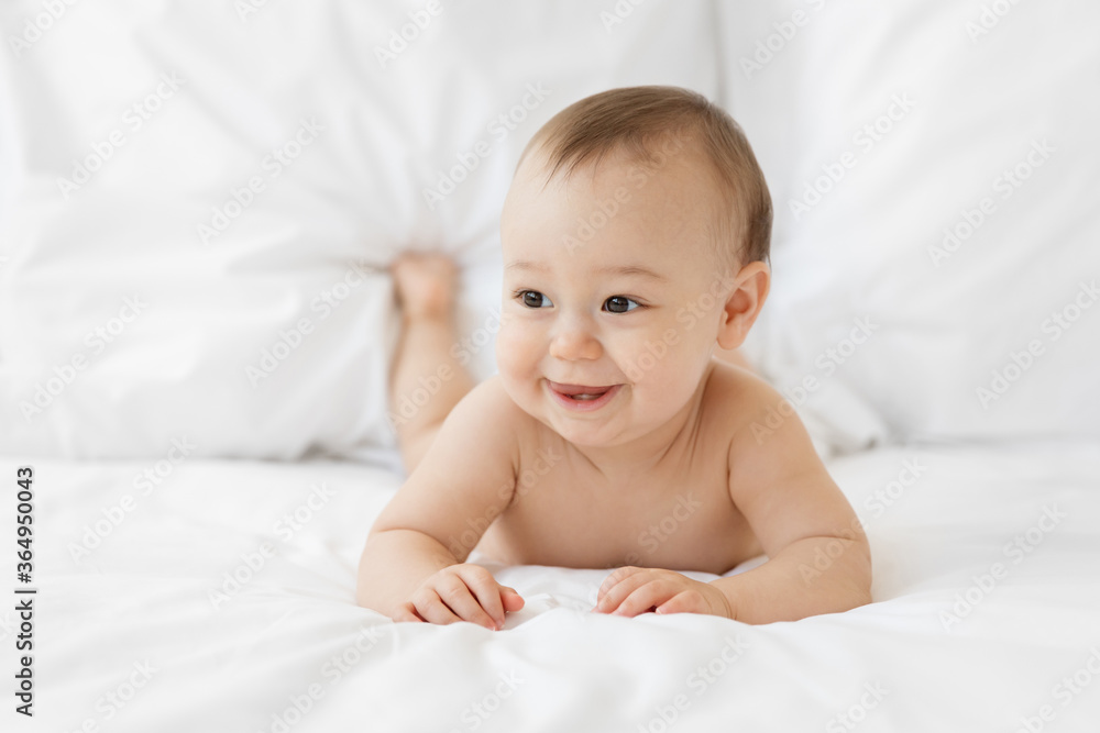 Cute smiling baby lying on stomach, on white bed Cute smiling baby lying on stomach, on white bed