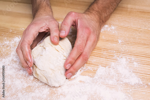 Man's hands working with dough on the wooden table