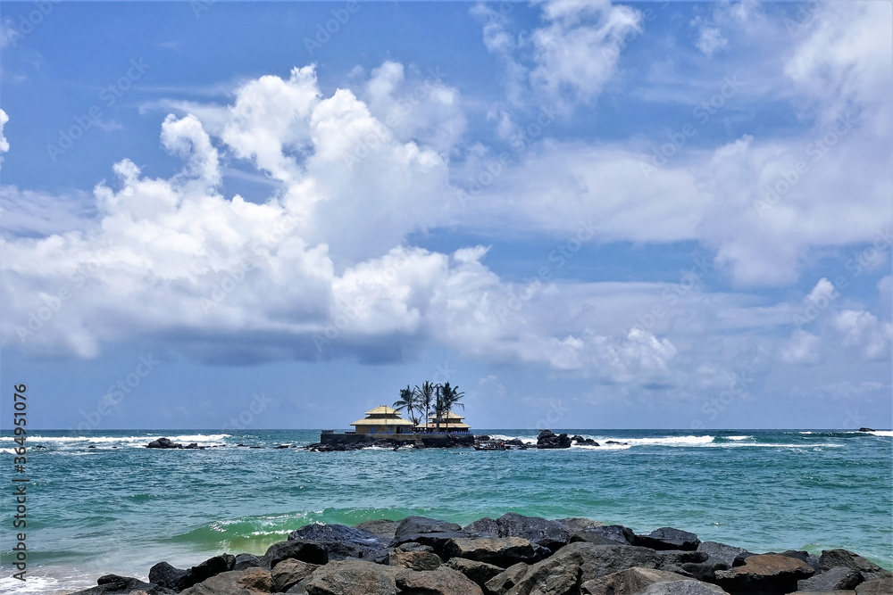 An amazing Buddhist temple in the Indian Ocean. On a tiny rocky island near the shore there is a small temple. Aquamarine waves beat against the rocks. Blue sky with picturesque clouds. Sri Lanka. 