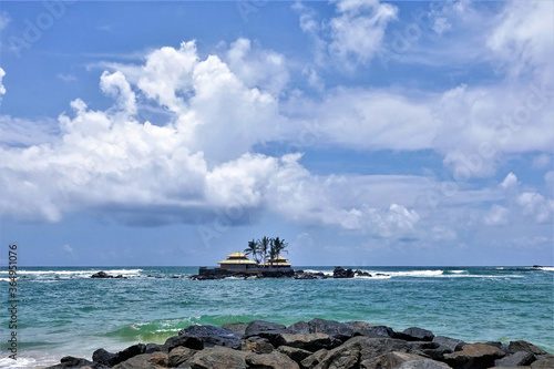 An amazing Buddhist temple in the Indian Ocean. On a tiny rocky island near the shore there is a small temple. Aquamarine waves beat against the rocks. Blue sky with picturesque clouds. Sri Lanka.  © Вера 