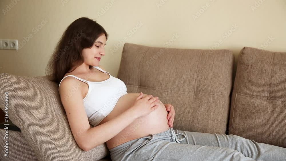 Portrait of caring mother strokes a naked pregnant tummy with two hands, on light room. A pregnant woman strokes a large belly in the sunny summer day Portrait of caring mother strokes a naked pregnant tummy with two hands, on light room. A pregnant woman strokes a large belly in the sunny summer day