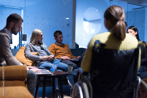 Handicapped young woman with colleagues working in office. She is smiling and passionate about the workflow. Performing in co-working space. Office people working together.