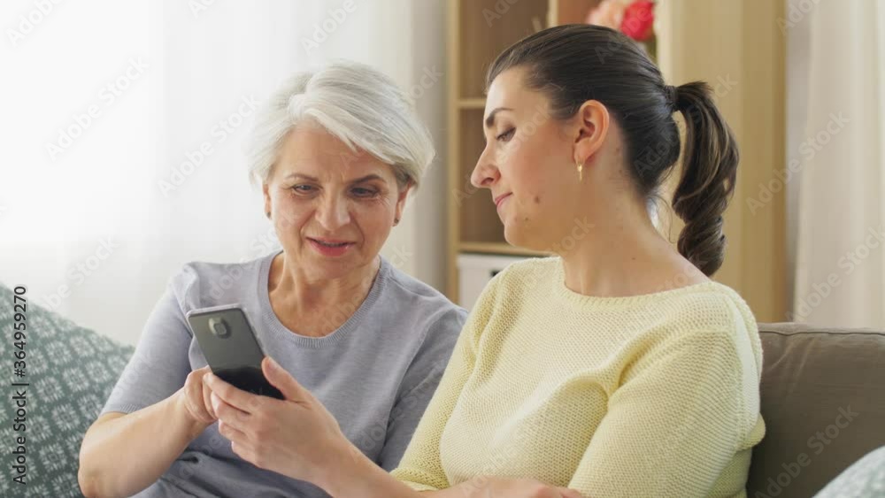 family, generation and technology concept - happy smiling senior mother and adult daughter with smartphone at home family, generation and technology concept - happy smiling senior mother and adult daughter with smartphone at home
