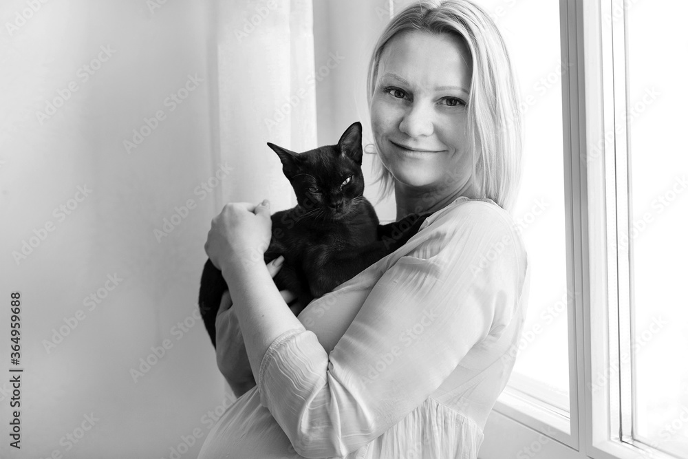 Beautiful woman and burmese kitten. A woman holds a kitten in her arms. Burmese cat at home. Bright interior in the kitchen.