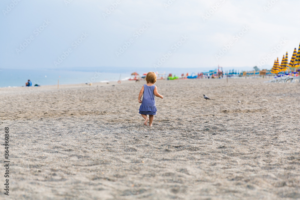 A little girl plays on the shore of the Mediterranian Sea in Sicily, Italy. The beach is empty due to a pandemic. Relaxation of quarantine and a walk along the sea.
A little girl plays on the shore of the Mediterranian Sea in Sicily, Italy. The beach is empty due to a pandemic. Relaxation of quarantine and a walk along the sea.