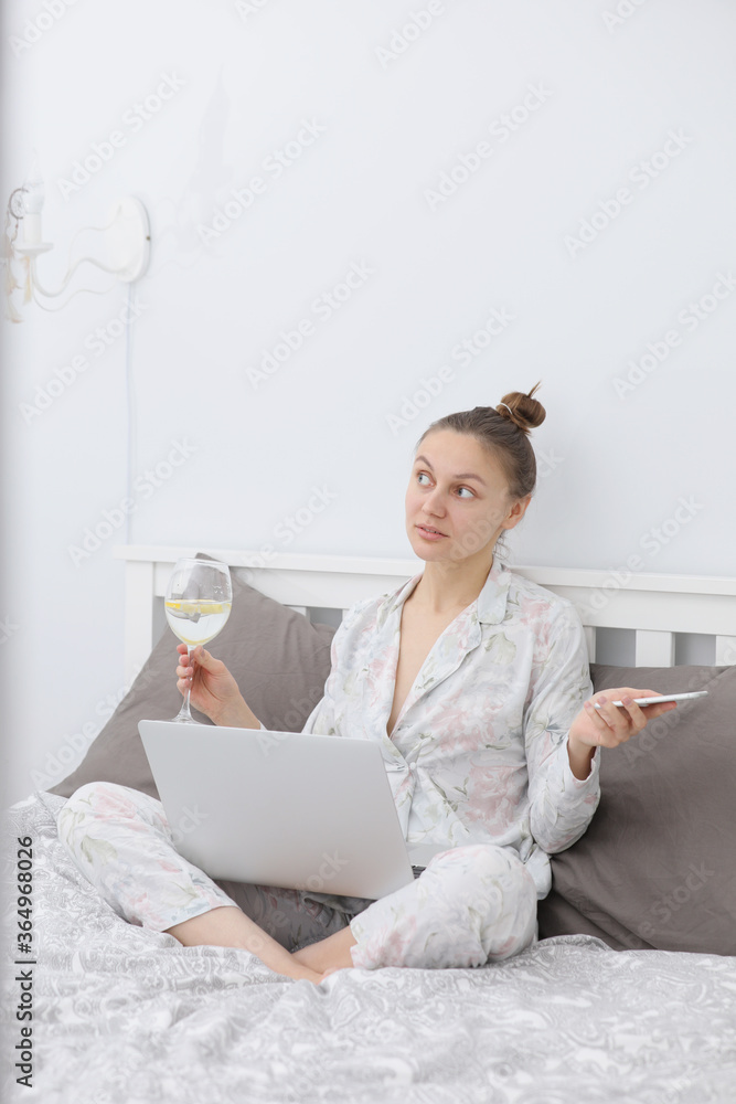 Young woman using her laptop while relaxing in bed and drinking wine. To stay home. Online study. Remote work. Young woman using her laptop while relaxing in bed and drinking wine. To stay home. Online study. Remote work.