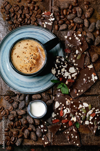 Cup of espresso coffee with jug of milk, handmade dark chocolate, coffee and cocoa beans around over dark ceramic tile as background. Flat lay, copy space © Natasha Breen
