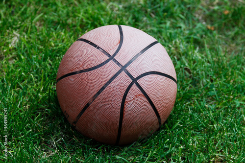 Basketball ball on the grass. Basketball ball waiting for children. Green grass and worn basketball ball.