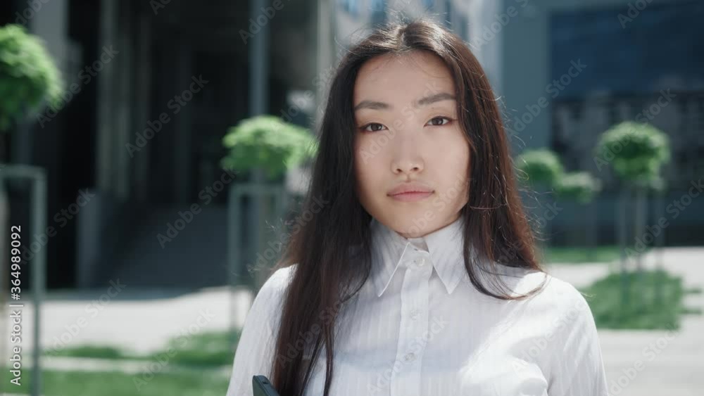 Gorgeous young beautiful asian business woman in formal wear looks at camera outside business district. Confident girl. Attractive people. Portraits. Gorgeous young beautiful asian business woman in formal wear looks at camera outside business district. Confident girl. Attractive people. Portraits.