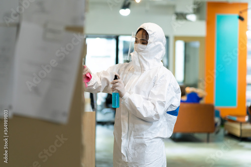 Asian woman in protective suit and mask disinfecting in office. Protection agsinst COVID-19 disease photo