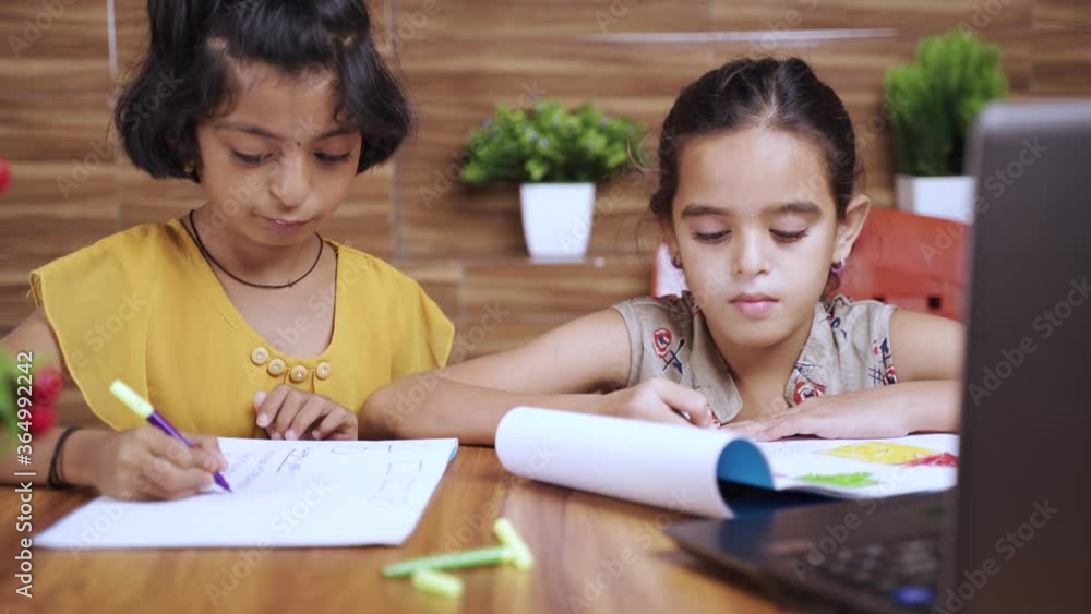 Two kids busy in writing by looking into the laptop during online or virtual class at home - concept of e-learning or distance learning or children's lifestyle during coronavirus or covid-19 pandemic. Two kids busy in writing by looking into the laptop during online or virtual class at home - concept of e-learning or distance learning or children's lifestyle during coronavirus or covid-19 pandemic.