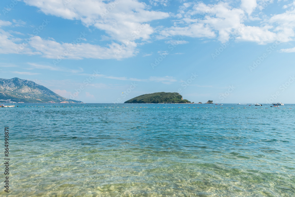 Shallow Adriatic sea coast with distant people, boats, island and mountains