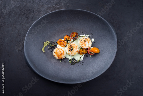 Traditional barbecue scallops with tomatoes, algae and Japanese furikake spice mix in a lemon coconut sauce offered as top view on a modern design plate with copy space