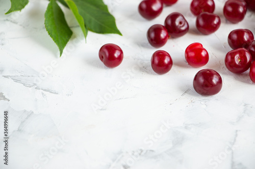 A bunch of cherry berries and green leaves on a light background along the top edge of the image. Copy space for text. Still life in a light key.