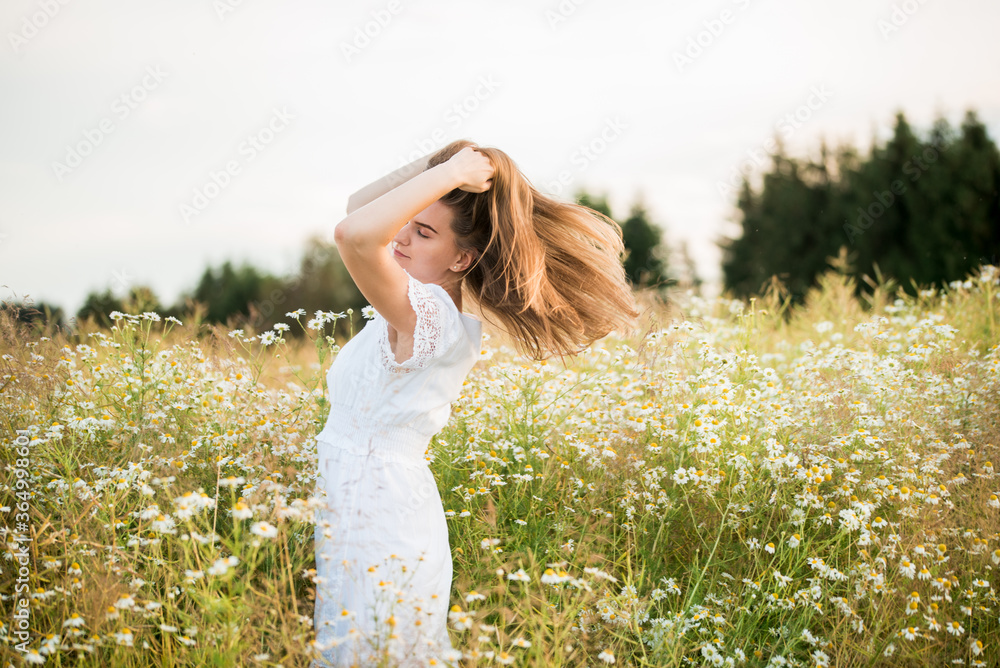 Obraz premium Happy girl on the camomile field, summer sunset. in a white dress. running and spinning, the wind in my hair, life style. freedom concept and hot summer