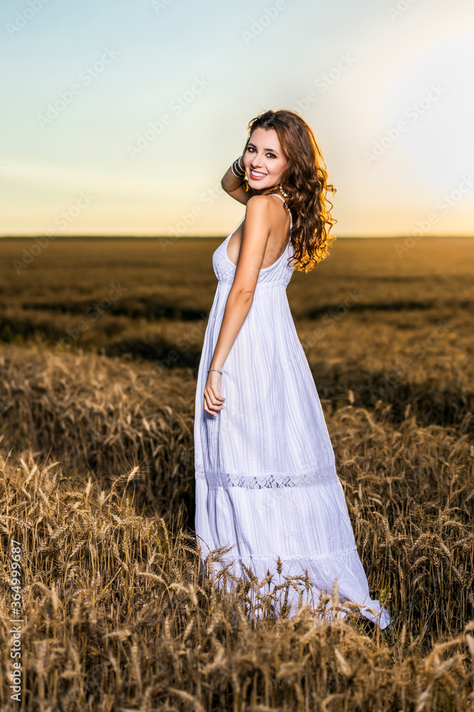 Obraz premium A beautiful woman in a white dress in a wheat field at sunset.