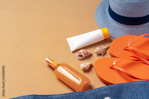 Beach bag with suntan products, flip-flops and hat on beige background