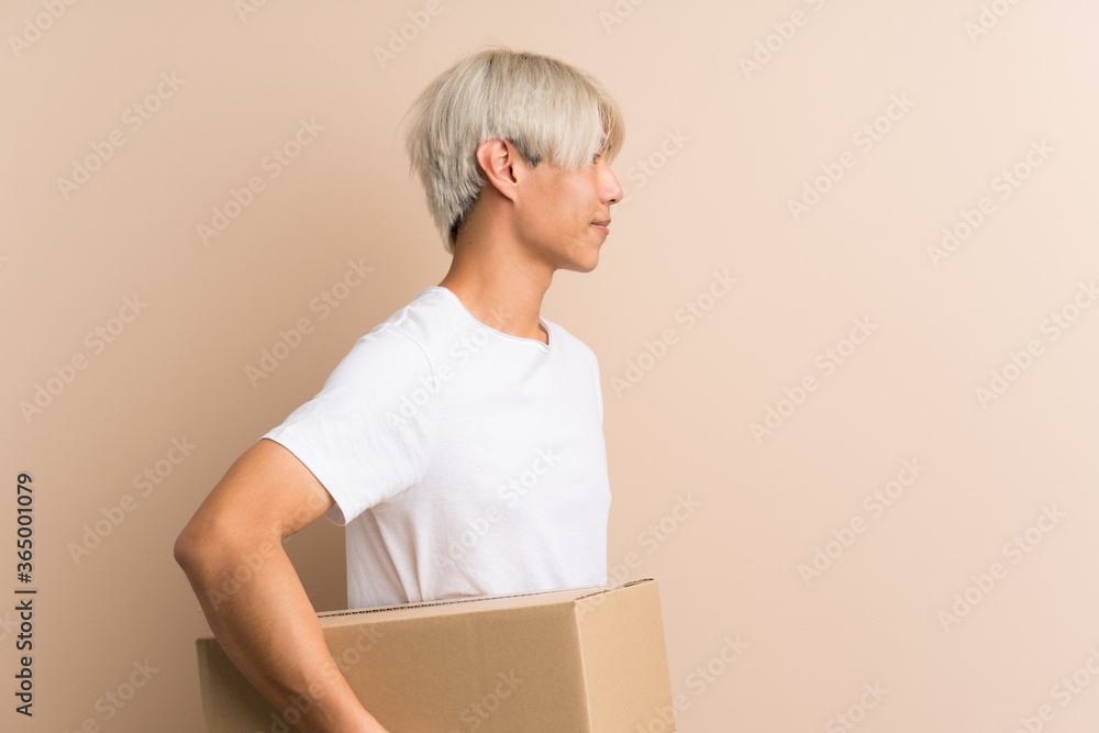 Young asian man over isolated background holding a box to move it to another site in lateral position Young asian man over isolated background holding a box to move it to another site in lateral position
