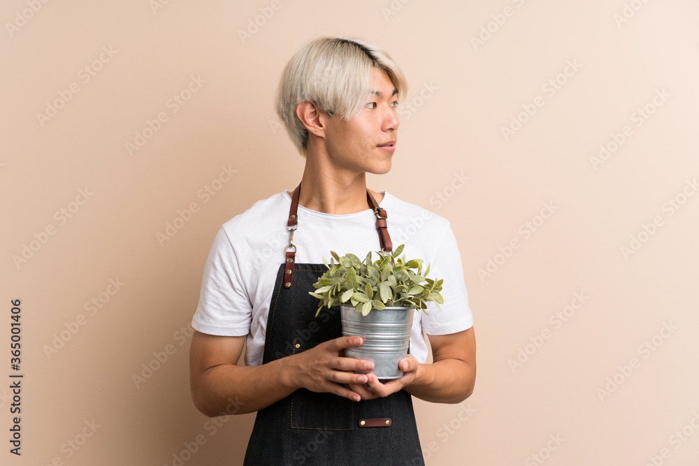Young asian man over isolated background taking a flowerpot Young asian man over isolated background taking a flowerpot