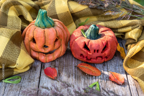 Two funny sculptures of autumn pumpkins among fallen leaves, dry grass and a yellow scarf. Halloween pumpkins for the holiday. photo