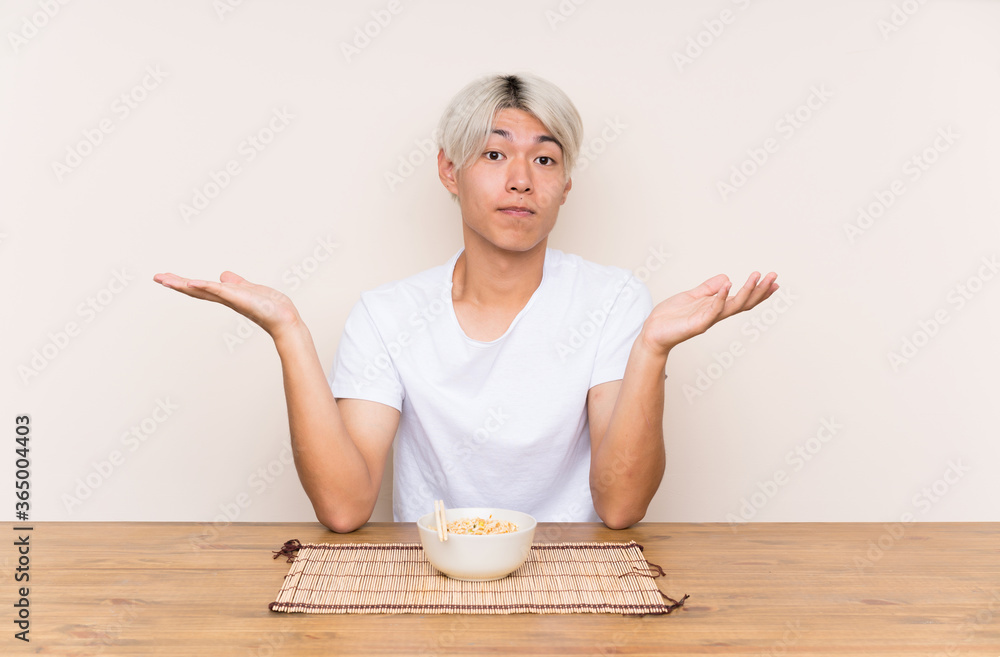 Young asian man with ramen in a table having doubts with confuse face expression Young asian man with ramen in a table having doubts with confuse face expression