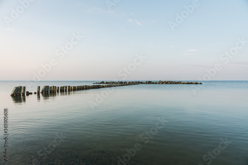 Calm morning sea surface with old stone pier and rocks. Morning seascape.