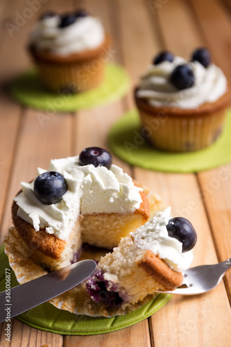 Homemade blueberry cup cake decorated with white cream and three blueberries lactose-free dessert, on natural wood 