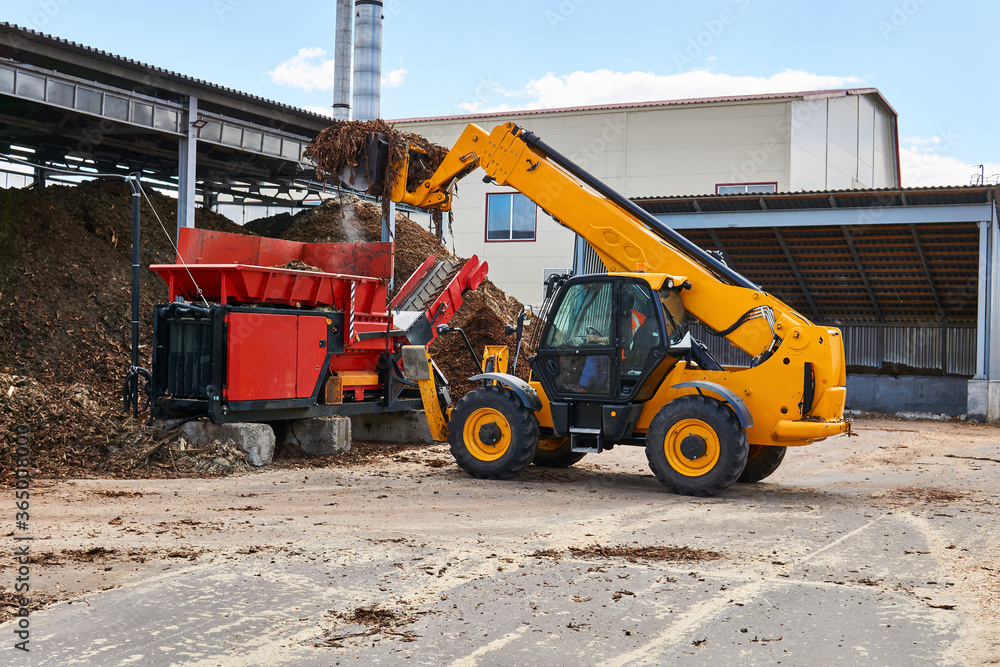 bucket loader loads tree bark into an industrial tree chipper bucket loader loads tree bark into an industrial tree chipper