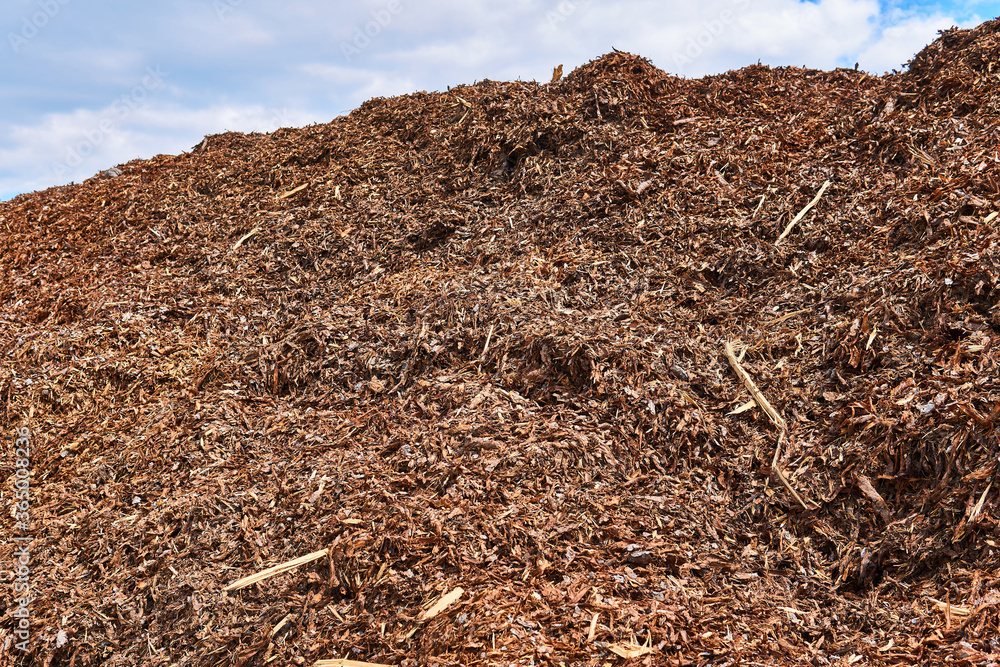 Fototapeta premium heap of tree bark removed from logs at a woodworking factory against sky