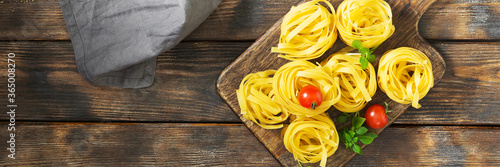 Fettuccine or tagliatelle pasta. Fettuccine or tagliatelle pasta on a wooden Board on a brown wooden table. Top view with a space for text. Cheese paste on the table. Banner with space for text